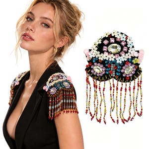 May include: A pair of black shoulder epaulets featuring floral embellishments, clear and pink faceted crystals, and sequins. The epaulets are adorned with long, dangling beaded fringe strands in red, yellow, and clear glass beads.
