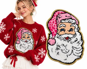 Puede incluir: Un suéter de punto rojo con patrones de copos de nieve blancos y un gran parche texturizado de Santa Claus con un gorro rosa de estampado de leopardo. El parche tiene una barba blanca, ojos azules y un borde de purpurina dorada.