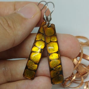 May include: Handmade earrings with a rectangular shape and a unique design. The earrings feature a gold and black pattern, with silver-colored ear wires. The design has a textured appearance, adding to their visual appeal. These earrings are a stylish accessory.