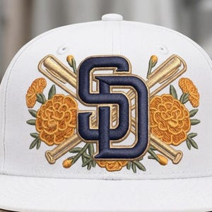 以下が含まれることがあります： 白い野球帽。紺色の「SD」の文字、交差した野球バット、オレンジ色のマリーゴールドの花が刺繍されています。帽子はつばが平らで、上部にボタンが付いています。