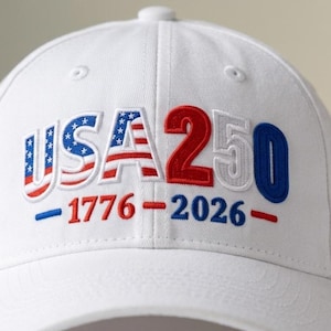 May include: White baseball cap with embroidered text and numbers. The text "USA 250" is in red, white, and blue, with the American flag incorporated into the "USA". The years "1776" and "2026" are also embroidered.