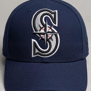 Puede incluir: Gorra de béisbol azul marino con un logotipo bordado. El logotipo es una letra "S" estilizada en blanco y negro con una rosa de los vientos y un diseño de béisbol en el centro. La gorra tiene una visera curva y un botón en la parte superior.