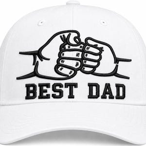 May include: White baseball cap with a black embroidered design of two fists bumping, with the text "BEST DAD" below. The cap has a curved brim and a button on top.