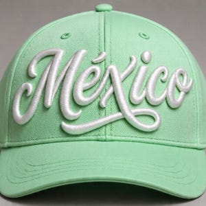 Puede incluir: Gorra de béisbol verde claro con la palabra "México" bordada en blanco en la parte delantera. La gorra tiene una visera curva y un botón en la parte superior.