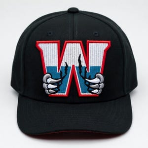 May include: Black baseball cap with a red brim. The cap features a large, embroidered "W" in red, white, and blue, with clawed hands grasping the letter. The cap is a fitted style.