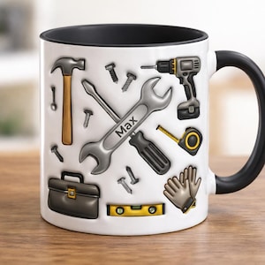 Puede incluir: Taza de cerámica blanca con interior y asa negros, decorada con diversas herramientas como un martillo, una llave y un taladro. La palabra "Max" está impresa en la llave. La taza está sobre una superficie de madera.