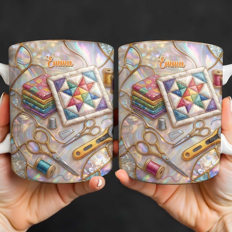 K&ouml;nnte beinhalten: Zwei wei&szlig;e Keramikbecher mit Quilt-Motiv. Jeder Becher zeigt einen bunten Quiltblock, Stoffstapel, Scheren und Garnrollen. Der Name "Emma" ist in Schreibschrift auf jedem Becher geschrieben.