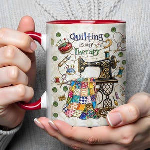 K&ouml;nnte beinhalten: Wei&szlig;er Keramikbecher mit rotem Innenraum und Henkel, mit einem N&auml;h-Themen-Design. Das Design umfasst eine Vintage-N&auml;hmaschine, einen bunten Quilt und den Text "Quilting is my Therapy."