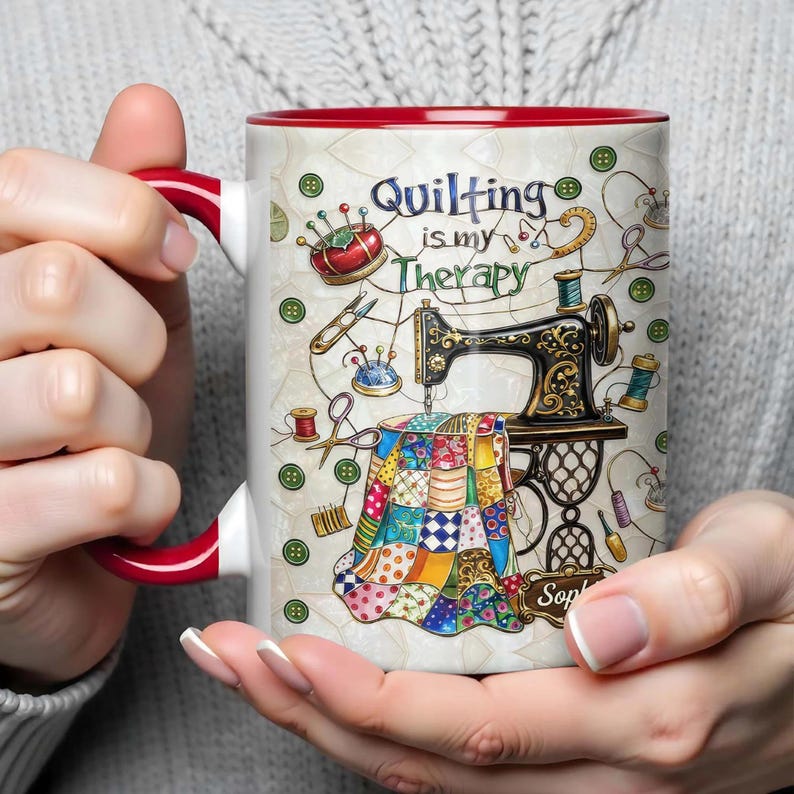 K&ouml;nnte beinhalten: Wei&szlig;er Keramikbecher mit rotem Innenraum und Henkel, mit einem N&auml;h-Themen-Design. Das Design umfasst eine Vintage-N&auml;hmaschine, einen bunten Quilt und den Text "Quilting is my Therapy."