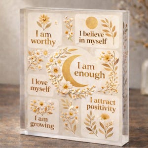 May include: A clear acrylic block with gold lettering and floral designs. The block displays motivational phrases such as "I am worthy," "I believe in myself," and "I am enough." The design includes a crescent moon and flower illustrations.