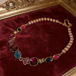 May include: A gold necklace with a mix of colourful gemstones and a strand of pink pearls. The necklace features various shapes and sizes of gemstones in shades of red, blue, green, and purple, set in gold bezels.