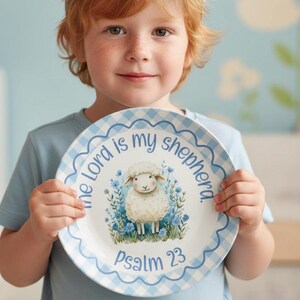Puede incluir: Un plato blanco con un borde de cuadros azules y el texto "El Señor es mi pastor" y "Salmo 23". El plato presenta una oveja de dibujos animados rodeada de flores azules.
