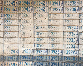 May include: A wall covered with vintage number plates from the 1970s. The plates are all from the state of Pennsylvania and feature a variety of numbers and letters. The plates are all in various states of wear and tear, with some being more faded than others.