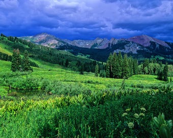 May include: A lush green valley with a small stream running through it. The valley is surrounded by mountains with a dark blue sky and clouds above.