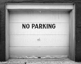 May include: A black and white photograph of a closed garage door with a sign that reads "NO PARKING".