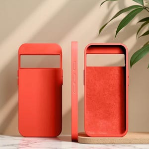 Puede incluir: Se muestran tres fundas rojas para teléfono. Las fundas están hechas de un material liso y tienen un diseño rectangular con un recorte para la cámara. Una funda se muestra de lado, revelando el grosor. Las fundas están diseñadas para proteger un teléfono.