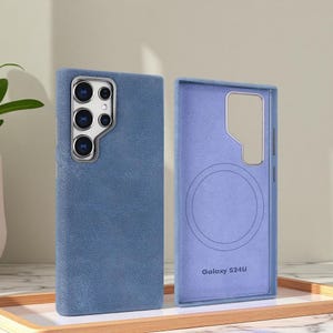 Puede incluir: Juego de dos fundas azules para teléfono. La funda exterior tiene un aspecto texturizado similar al denim, con un recorte plateado para la cámara. La funda interior es azul claro con un diseño circular y el texto "Galaxy S24U".