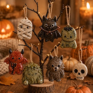May include: Seven ceramic Halloween ornaments hanging from a dark tree branch. The figures include a white mummy, a black bat, a green monster, a red devil with a pitchfork, a green swamp creature, a brown werewolf, and a white skull, all with twine.