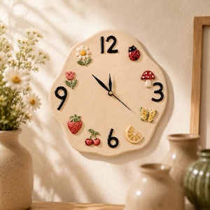 May include: A beige, irregularly shaped wall clock featuring black numerals at the 12, 3, 6, and 9 o'clock positions. The clock face is decorated with small, raised ceramic figures including a daisy, tulip, ladybug, mushroom, butterfly, lemon slice, strawberry, and cherries.