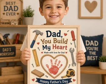 May include: A framed print featuring the text "Dad, You Build My Heart" and "Happy Father's Day" with illustrations of a hammer, screwdriver, wrench, ruler, tape measure, and wood block surrounding a central red handprint inside a heart shape.