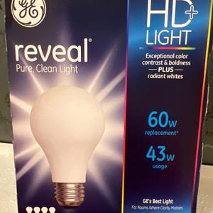 Puede incluir: Una caja azul marino de bombillas GE Reveal HD+ Light. La caja muestra una imagen de una bombilla y texto como "Reveal", "Pure, Clean Light", "HD Light" y "Enhanced Spectrum Halogen Bulbs". La caja contiene 4 bombillas.