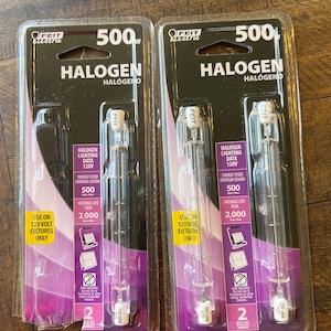 Puede incluir: Dos paquetes de bombillas halógenas Feit Electric de 500W. Cada paquete contiene dos bombillas y presenta un diseño negro y morado con información del producto y el texto "HALOGEN". Las bombillas son transparentes y cilíndricas.