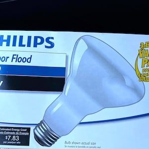 May include: A white Philips Indoor Flood BR30 65W light bulb package. The box has the text "3 Bulb Value Pack" and "Paquete Economico de 3 Bombillas". The package also shows the estimated energy cost.