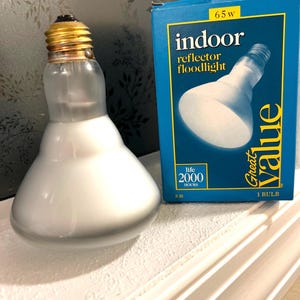 May include: A frosted glass R30 reflector floodlight bulb with a gold base sits next to a blue box. The box reads "indoor reflector floodlight" and "Great Value". The bulb is 65 watts and has a life of 2000 hours.