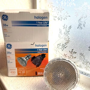 Puede incluir: Dos cajas de focos halógenos de interior GE, 38W, 490 lúmenes, con una vida útil de 1 año. Una sola bombilla halógena está junto a las cajas. Las cajas tienen el texto "halogen" y "1 Year Life".