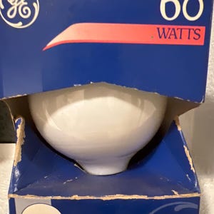 May include: A GE brand 60 watts light bulb in a blue cardboard box. The packaging features the GE logo, the text 60 WATTS, and a graphic showing a 9.5 cm diameter bulb with the text CULOT MOYEN and 1 AMPOULE printed on the front lower section.