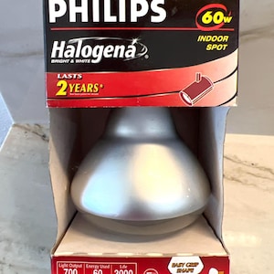 May include: A Philips Halogena indoor spot light bulb in its original packaging. The box is black and red with the brand name and product details. The bulb is silver and has a unique shape. The box indicates the bulb lasts 2 years.