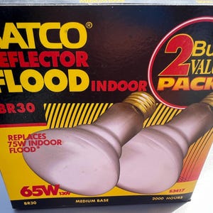 May include: A box of two SATCO reflector flood light bulbs. The box is black and yellow with red and yellow text. The bulbs are a light pink color with a medium base. The box reads "2 Bulb Value Pack".