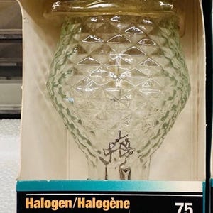 Puede incluir: Una bombilla Sylvania Crystal MB19 en su embalaje original. La bombilla de vidrio transparente tiene un patrón texturizado en forma de diamante. El embalaje incluye el texto "Halogen/Halogène Crystal" y "Brilliant White Light". La bombilla es de 75 vatios.