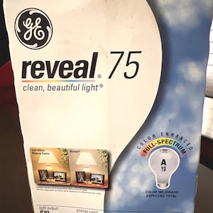 May include: A box for GE Reveal 75 light bulbs. The box is white with the GE logo and the words "reveal 75 clean, beautiful light." It also features a graphic of a light bulb and the words "Color Enhanced Full Spectrum."