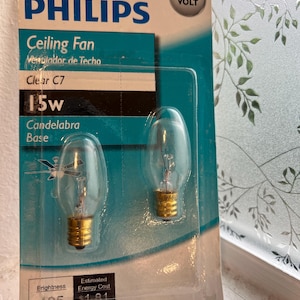 Op de afbeelding: Een Philips-verpakking met twee heldere C7 15w gloeilampen met een kaarsfitting. De verpakking is blauw en wit, gemarkeerd met 120 volt, en toont technische specificaties waaronder 105 lumen en de geschatte energiekosten.