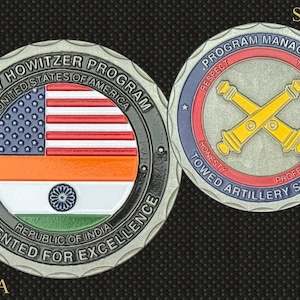 May include: A silver coin featuring the flags of the United States and India, with text reading "M777 Howitzer Program" and "Presented for Excellence." The reverse side displays crossed cannons and the words "Program Manager."