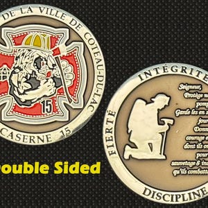 May include: Double-sided coin featuring the text "SERVICE INCENDIE DE LA VILLE DE COTEAU-DU-LAC" and "CASERNE 15". One side has a firefighter emblem, the other a kneeling figure with text. The coin is silver and gold with red accents.