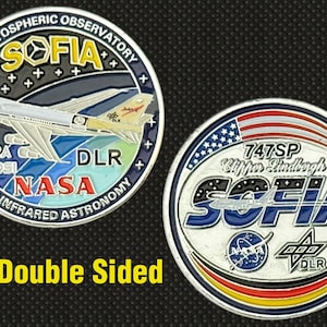 May include: Double-sided SOFIA commemorative coin. One side features a plane graphic with NASA and DLR logos, the other side displays the American flag and the text "747SP Clipper Lindbergh". The coin also has the text "Stratospheric Observatory".