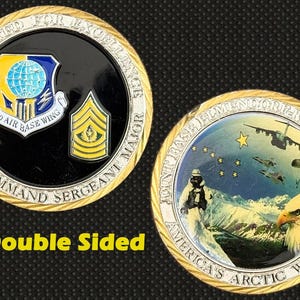 Puede incluir: Moneda de doble cara con borde dorado. Un lado presenta un emblema militar y el texto "6730 Air Base Wing Command Sergeant Major". El otro lado muestra un paisaje nevado, un águila y el texto "America's Arctic Warriors."