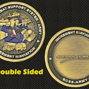 May include: Double-sided gold-colored coin with black and blue accents. One side features text and military-themed graphics, including a star and vehicles. The other side has text that reads "Northrop Grumman".