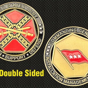 Puede incluir: Moneda de doble cara del Ejército de los Estados Unidos. Un lado presenta espadas cruzadas y cadenas dentro de un diseño rojo y dorado, con el texto "SUSTAIN SUPPORT DEFEND". El otro lado muestra una bandera roja con estrellas.