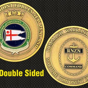 May include: Double-sided gold-colored coin featuring the text "HEADQUARTERS JOINT FORCES NEW ZEALAND" and "COMMAND WARRANT OFFICER MARITIME COMPONENT COMMANDER". The coin has a maritime theme with an anchor and flag design.