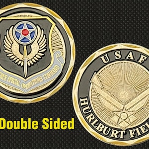 Puede incluir: Moneda conmemorativa de doble cara con detalles dorados y negros. Un lado presenta el emblema del Comando de Operaciones Especiales de la Fuerza Aérea, el otro el emblema de la USAF y "Hurlburt Field, FL".
