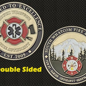 Könnte beinhalten: Doppelseitige Münze mit dem Logo der South Whatcom Fire Authority. Eine Seite zeigt ein Feuerwehr-Emblem mit einem medizinischen Symbol, die andere Seite zeigt eine Berglandschaft. Die Münze hat goldene, rote, schwarze und weiße Akzente.