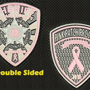 May include: Double-sided pink and silver commemorative coin. One side features the words "Sheriff" and "Deputy Sheriff" with a star and the words "Honesty, Loyalty, Unity, Colorado." The other side says "Pink Patch Project" with a pink ribbon.