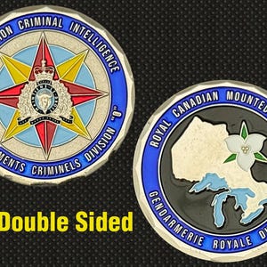 Może przedstawiać: Dwustronna moneta z emblematem "O" Division Criminal Intelligence z motywem gwiazdy i tekstem. Na odwrocie widnieje emblemat Królewskiej Kanadyjskiej Policji Konnej z mapą Kanady i białym kwiatem.