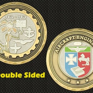 May include: Double-sided coin with a gold and silver finish. One side features a cartoon coyote holding a sign, the other side displays a crest with text "Aircraft Engineers". The coin has a gear-like border.