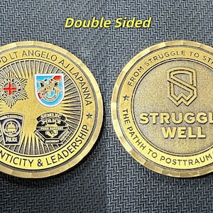 Op de afbeelding: Een dubbelzijdige, bronskleurige munt. Eén kant toont tekst en emblemen, waaronder "AUTHENTICITY & LEADERSHIP". De andere kant luidt "STRUGGLE WELL" met de tekst "FROM STRUGGLE TO STRENGTH" en "THE PATHH TO POSTTRAUMATIC GROWTH."