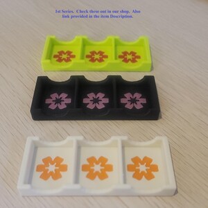 May include: Three rectangular organizers with three compartments each, in lime green, black, and white. Each compartment features a six-petaled flower graphic. Text at the top reads: 1st Series. Check these out in our shop. Also link provided in the item Description.