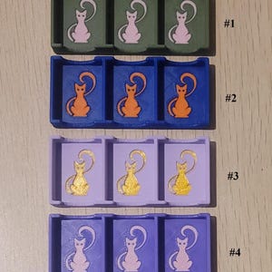 May include: Four rectangular plastic organizers, each featuring three compartments with a cat silhouette graphic. Row #1 is olive green with pink cats, #2 is blue with orange cats, #3 is light purple with gold cats, and #4 is purple with pink cats.